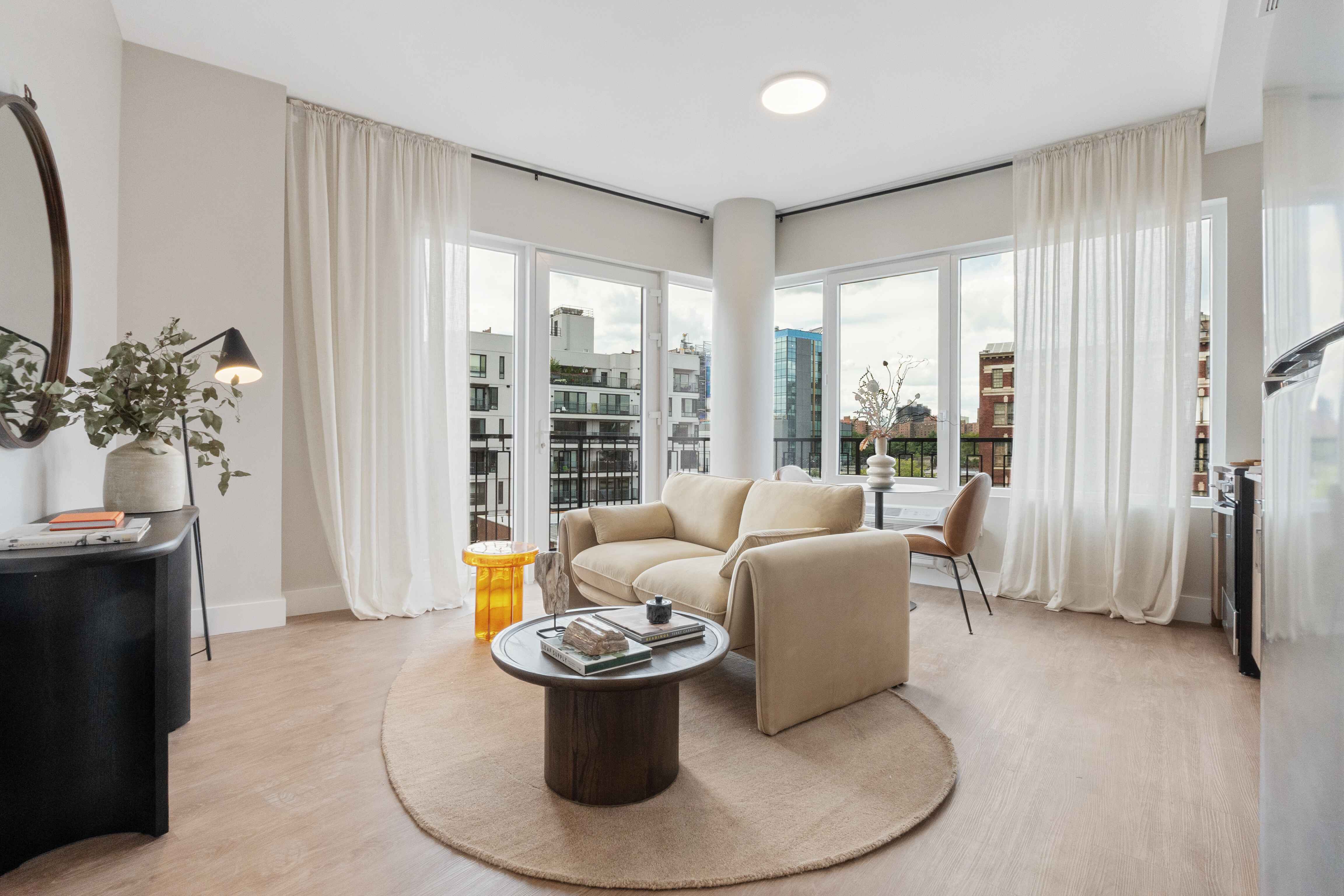 A bright, sunlit living room in an Astelle residence, with floor-to-ceiling windows and a city view.