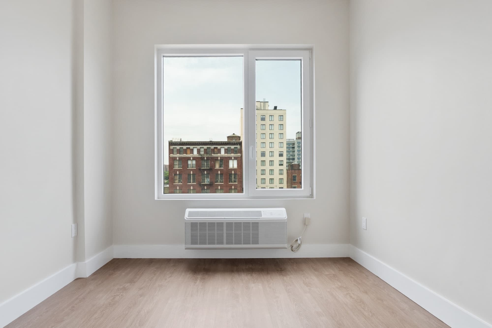 A one-bedroom residence at The Astelle, a sunlit bedroom with wide windows looking out over the South Bronx