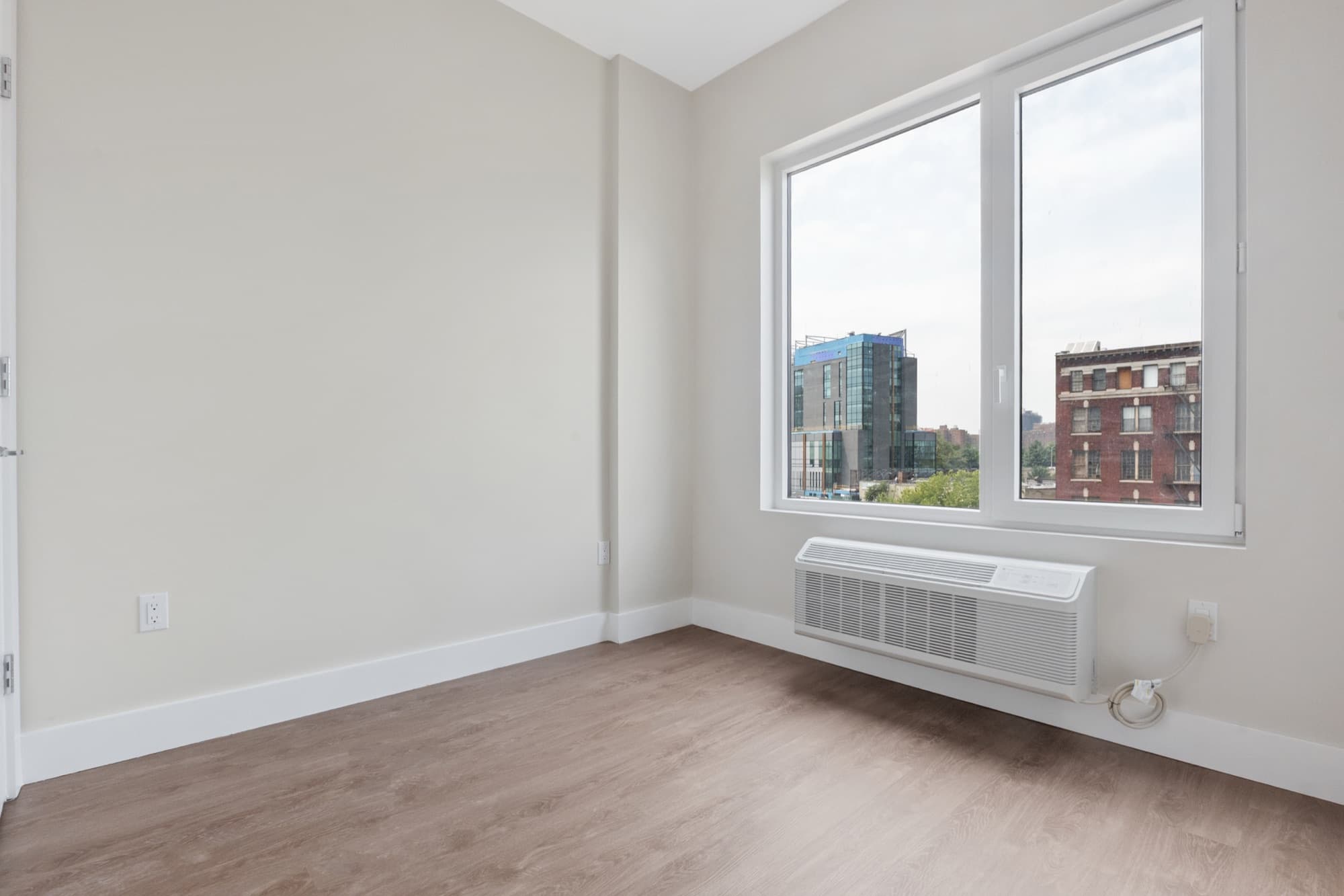 A residence at The Astelle, a sunlit bedroom with wide windows looking out over the South Bronx